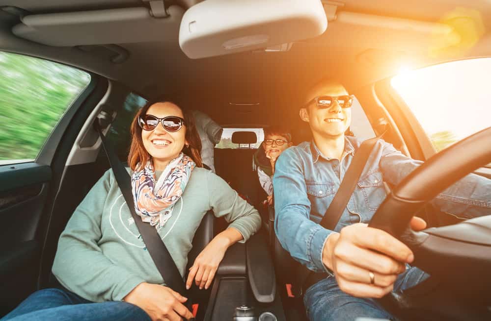 Holiday Travel Car Maintenance Checklist | C&M Auto Service, Inc. | Morgan Hill, CA. Image of young modern family driving in car with sun shining happy.