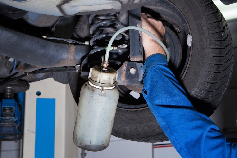 Why You Shouldn’t Overlook Brake Fluid Flushes During Routine Maintenance in Morgan Hill, CA, with C&M Auto Service. A man repairs a car tire while preparing for a brake fluid flush, ensuring vehicle safety and performance.