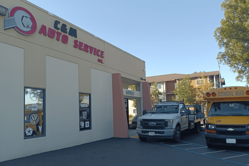 auto repair costs, auto repair in Morgan Hill, CA at C&M Auto Service Inc., Exterior view of C&M Auto Service Inc. building with a flatbed truck and a yellow school bus parked in front on a clear day.
